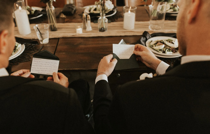 Two guests in formal attire reading custom handwritten place card notes at boho chic Colorado barn wedding reception table