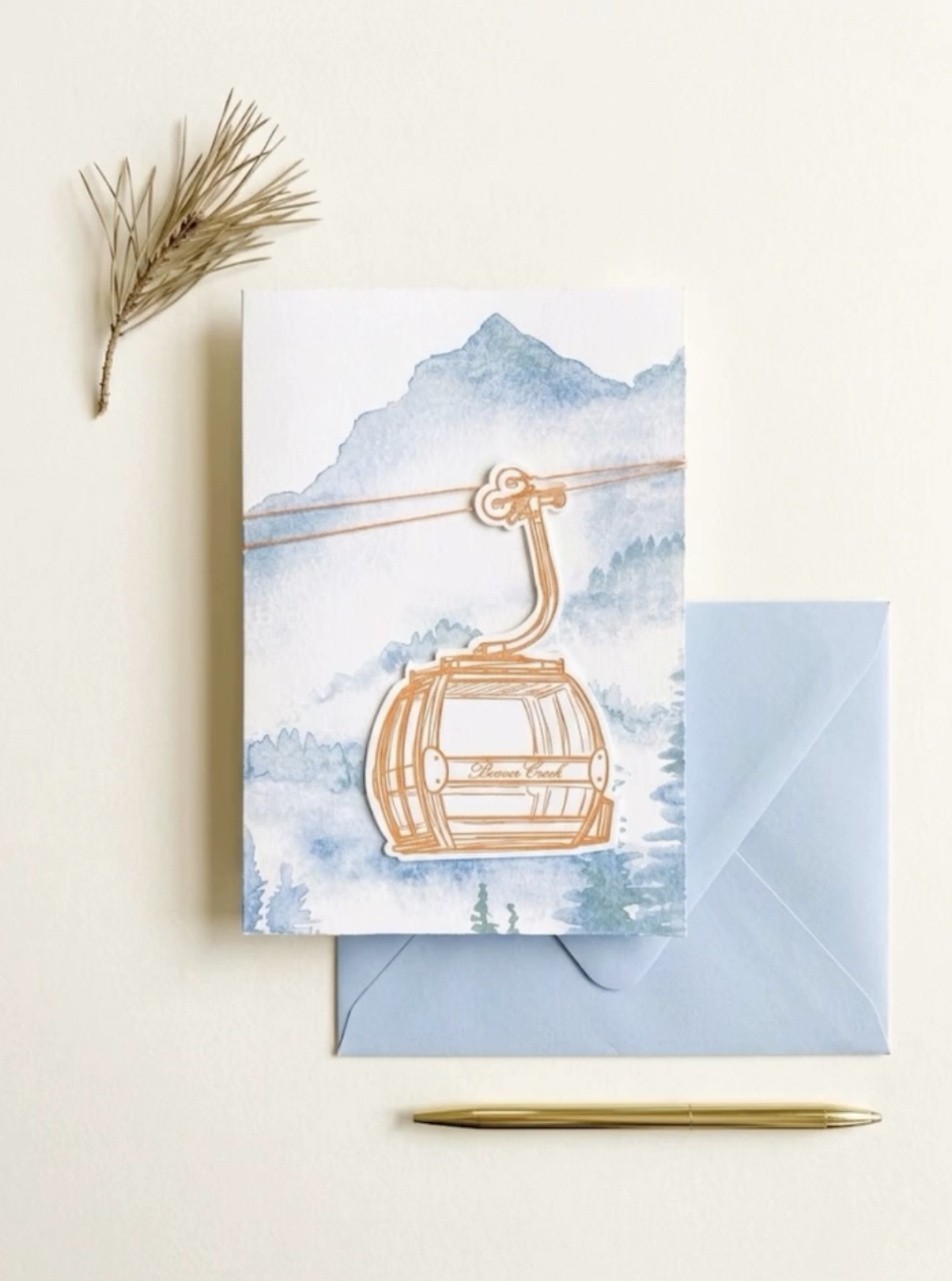 Mountain gondola wedding invitation card with watercolor alpine landscape, gondola die cut card with cord belly band, and light blue envelope, for an elegant Rocky Mountain destination wedding suite.